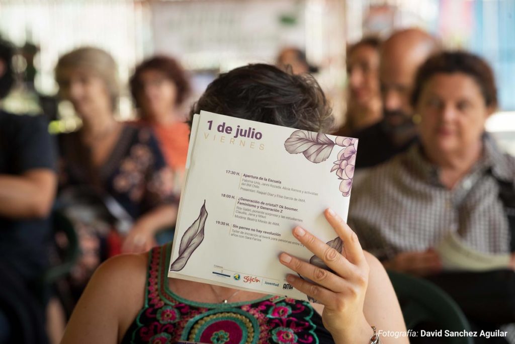 Mujer sosteniendo el libreto de la III Escuela Feminista de Ama Asturies, diseñado, maquetado e ilustrado por Eva Cortés