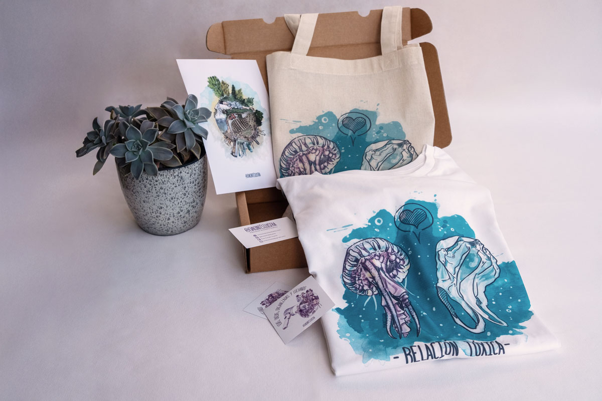 En la imagen se ve un ejemplo del pack de productos de temática feminista "ecologista". En la imagen se puede observar una lamina DIN A5 con una de las ilustraciones que reflexionan sobre nuestro planeta de Eva Cortés, una totebag y una camiseta de la misma línea.